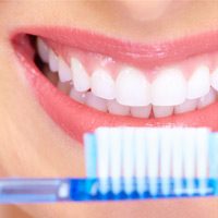 A full smile with white teeth and a blue toothbrush in front of the smile