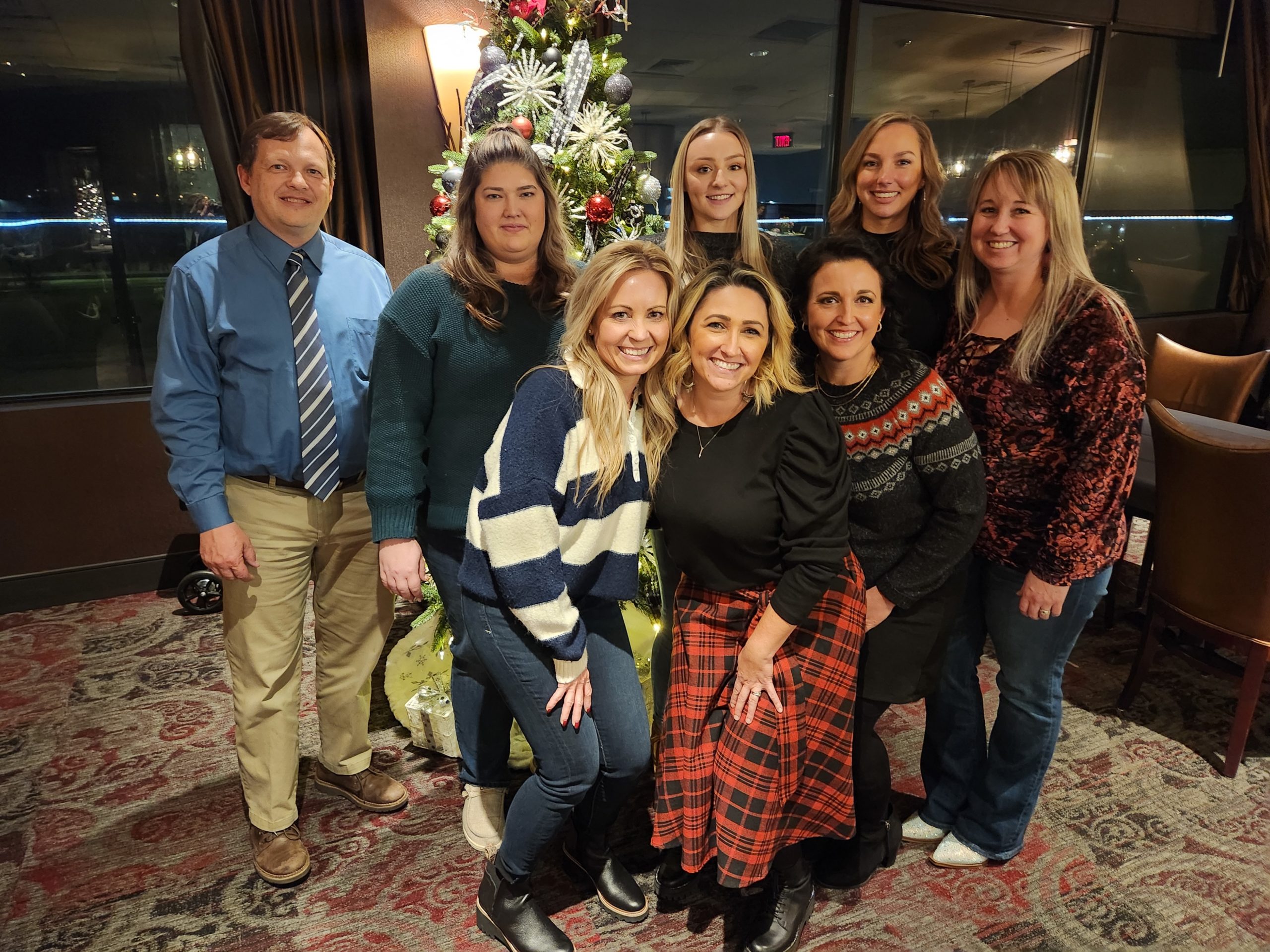 The entire dental team of Fourth Street Family Dental posing together in front of a Christmas tree in a high rise building in Hermiston, OR